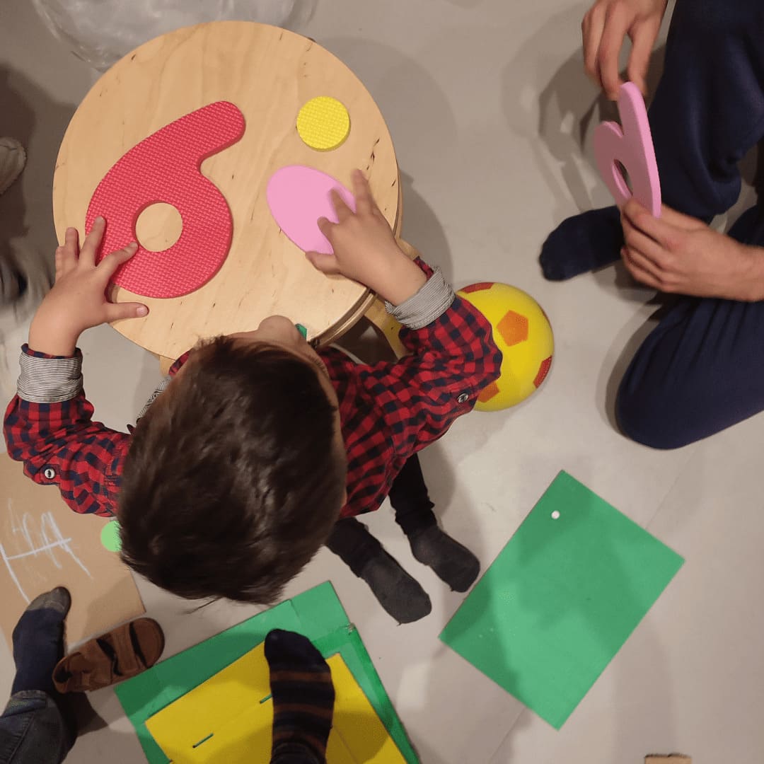 Niño con números de goma eva en una sesión de arteterapia, le vemos desde arriba apoyado en una mesa circular