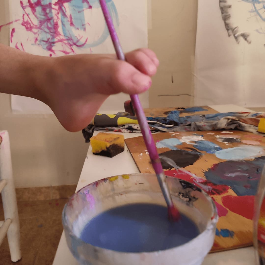 Niño sujetando un pincel con el pie durante una sesión de Arteterapia para personas con movilidad reducida