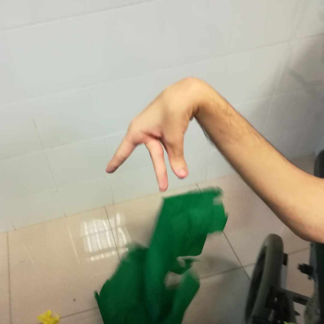 Sesión de arteterapia para adultos, vemos la mano del paciente dejando caer un trozo de papel verde.